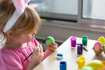 Little girl in easter bunny ears painting colored eggs. easter family holiday celebration at home.