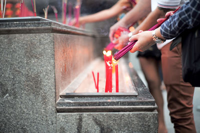 Closeup hands holding the bundle of incenses for lighting with candles in the sand tray