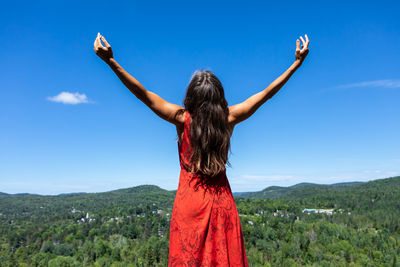 Rear view of woman with arms raised against blue sky