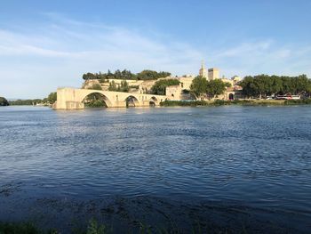 Arch bridge over river by buildings against sky