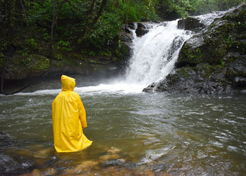 Rear view of boy wearing raincoat against waterfall