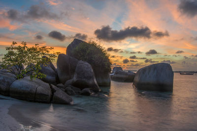 Rocks by sea against sky during sunset