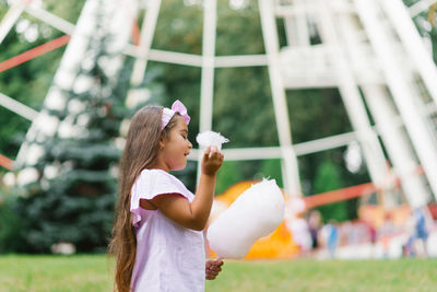 Child girl in an amusement park in the summer eats cotton candy and smiles happily