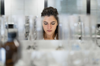 Concentrated young professional female scientist working at table with glass flasks while conducting research in medical lab