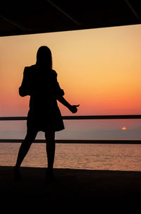 Silhouette man standing on beach against orange sky