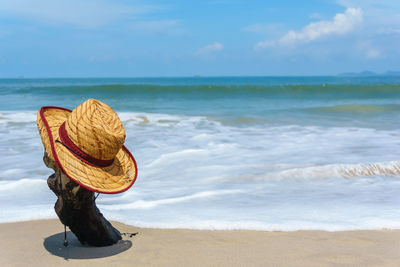 Hat on driftwood at beach against sky