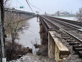 Railroad tracks by river in city against sky