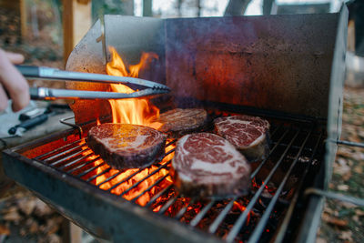 Close-up of hand grilling meat on barbecue grill