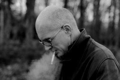 Side view of man smoking cigarette in forest