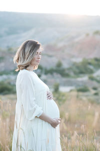 Pregnant woman holding belly standing on field