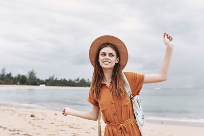 Young woman standing at beach against sky