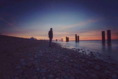 Side view of man standing at beach against sky during sunset