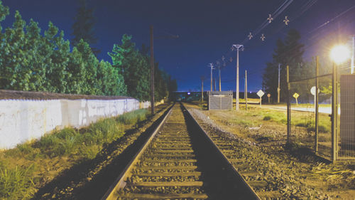 Railway tracks amidst trees against sky at night