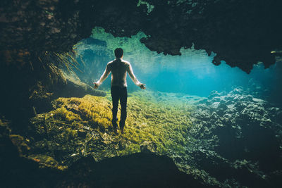 Rear view of man standing on rock in sea