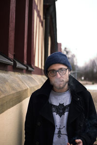 Portrait of young man smoking cigarette while standing by wall