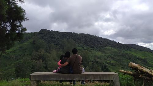 Rear view of people sitting on mountain against sky