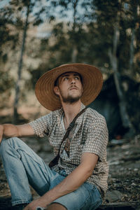 Portrait of man wearing hat sitting against trees