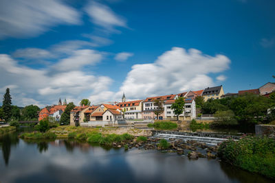 Houses by river and buildings against sky