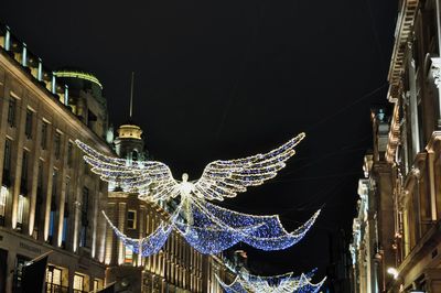 Low angle view of illuminated christmas decoration against building and sky at night