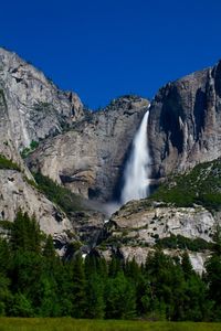 Low angle view of waterfall against clear blue sky