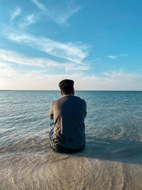 Rear view of man standing at beach against sky