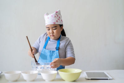 A cute asian kid is learning sweets, she is pouring the ingredients together. your home kitchen