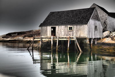 Wooden house by lake against sky