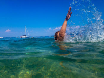Mid adult woman with hand raised swimming in sea against blue sky during sunny day