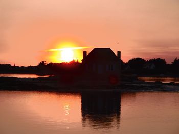 Silhouette houses in front of river against romantic sky at sunset