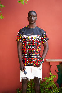 Content african american male in casual wear looking at camera against red background on street with plants