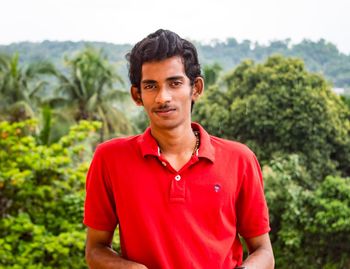 Portrait of man wearing red t-shirt against trees