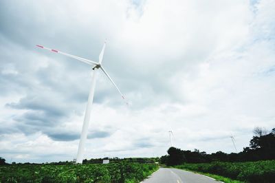 Wind turbines on land against cloudy sky