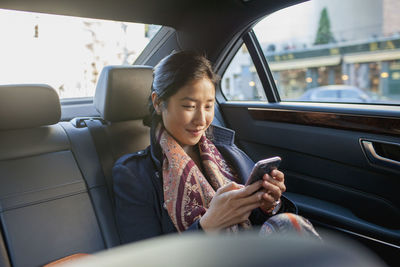 Young asian businesswoman looking at smartphone sitting in car service limousine