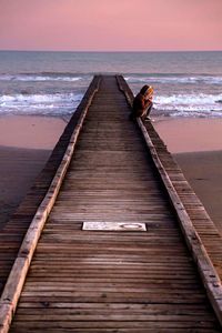 Boardwalk on beach against sky during sunset