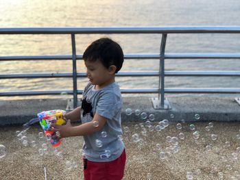 High angle view of boy playing with squirt gun while standing on promenade during sunset