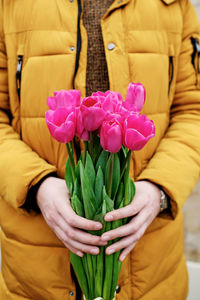 Blond man in a yellow winter jacket with a bouquet of tulips in hands