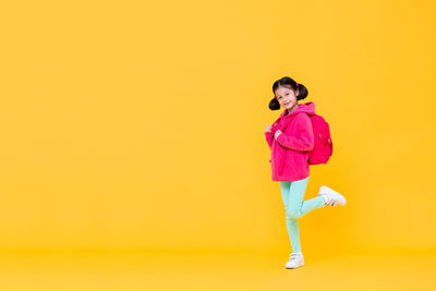 Portrait of young woman standing against yellow background