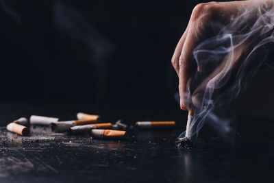 Cropped hand of person holding cigarette against black background