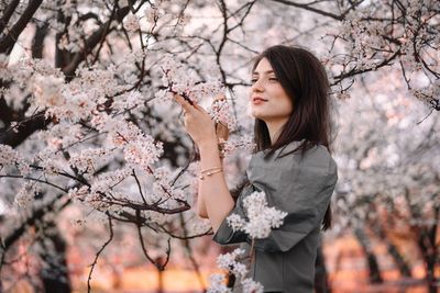 Full length of woman standing by cherry blossom tree