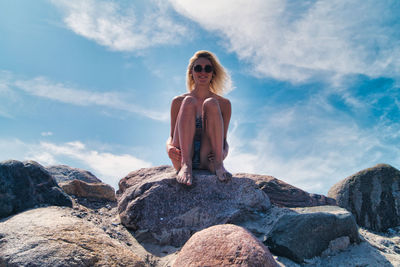 Woman sitting on rock against sky