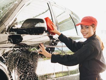 Portrait of smiling young woman cleaning car in workshop