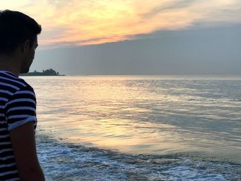 Boy standing in sea against sky during sunset