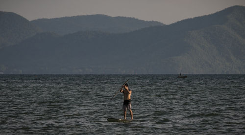 Man paddleboarding in sea against sky