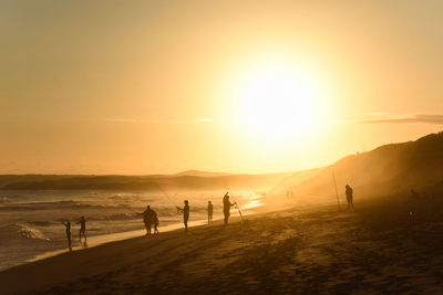 Silhouette people on beach against sky during sunset