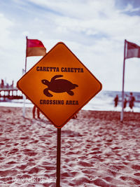 Close-up of warning sign on beach against sky