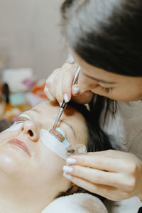Girl cosmetologist laminates and paints woman eyelashes
