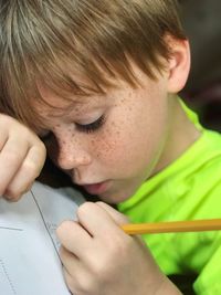Close-up of boy writing in book with pencil
