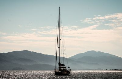 Sailboat sailing on sea against mountains