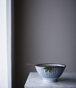 Chopsticks and maple leaf on bowl on table against wall