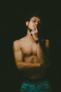 Rear view of shirtless young woman standing against black background